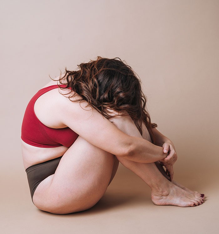 Young unhappy woman plus size in underwear sitting in closed pos
